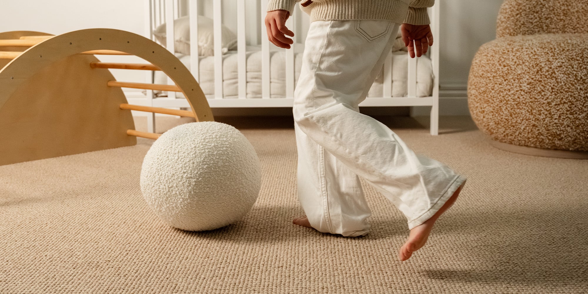 A child stepping across a soft, natural wool Cotswold carpet in a warm, sunlit nursery
